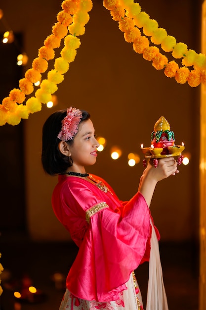 写真 ディワリ祭のお祝いのためにdiyaまたは石油ランプを保持しているかわいいインドの少女。