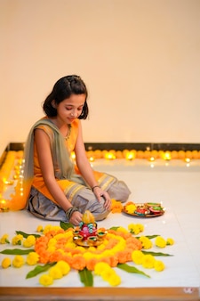 Bambina indiana carina che fa decorazioni con fiori e lampada a olio per il festival di diwali a casa.