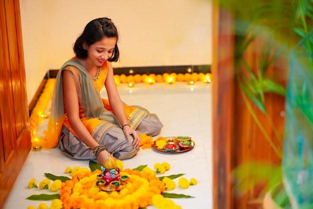 自宅でディワリ祭のために花と石油ランプで装飾を作るかわいいインドの少女。