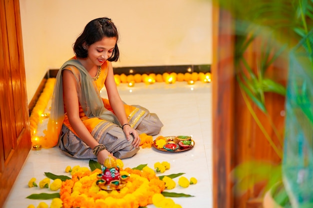 Cute indian little girl making decoration with flower and oil lamp for diwali festival at home