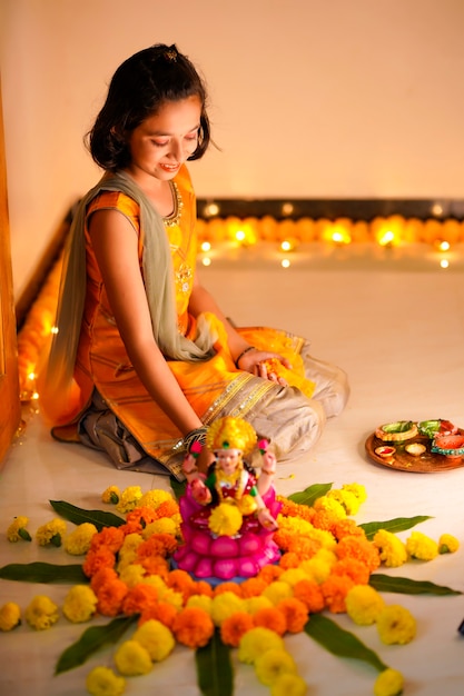 Cute indian little girl making decoration with flower and oil lamp for diwali festival at home