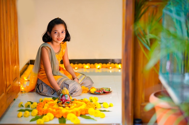 Bambina indiana carina che fa decorazioni con fiori e lampada a olio per il festival di diwali a casa.