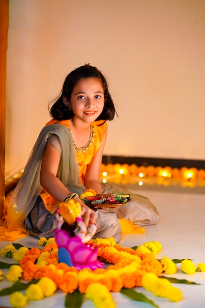 Cute indian little girl making decoration with flower and oil lamp for diwali festival at home.