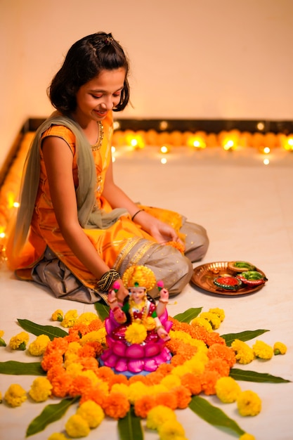 Cute indian little girl making decoration with flower and oil lamp for diwali festival at home.