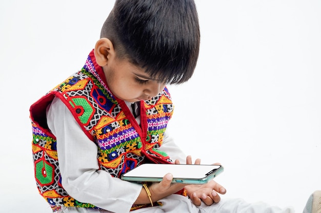 Cute indian little kid in ethnic dress playing with phone or showing phone screen and expression on white background
