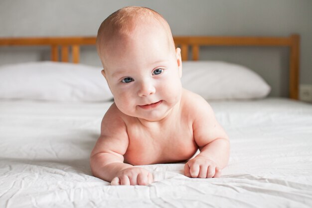 Cute infant baby looking at camera on a white bed. 