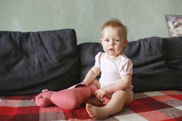 Фото Милая маленькая девочка сидит в одиночестве на красном клетчатом одеяле, играя с мягкими игрушками