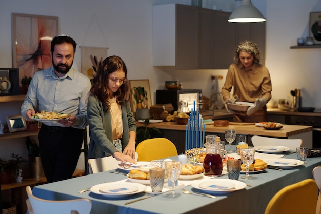 Милая еврейская девушка помогает своим родителям обслуживать стол домашней едой