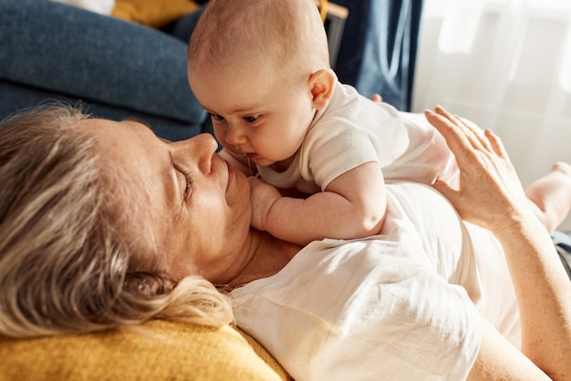 A cute joyful baby and his grandmother are lying on the floor in a bright cozy room happy childhood