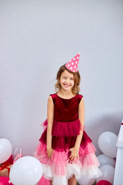 Foto bambina gioiosa carina in abito rosa e cappello gioca con palloncini a casa stelle filanti festa di compleanno buon compleanno festeggiando