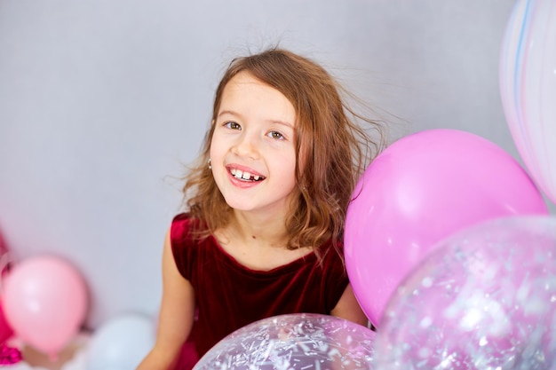 Cute Joyful little girl in pink dress and hat play with balloons at home birthday party