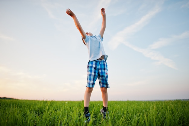 Cute jumping boy in green grass field at evening.