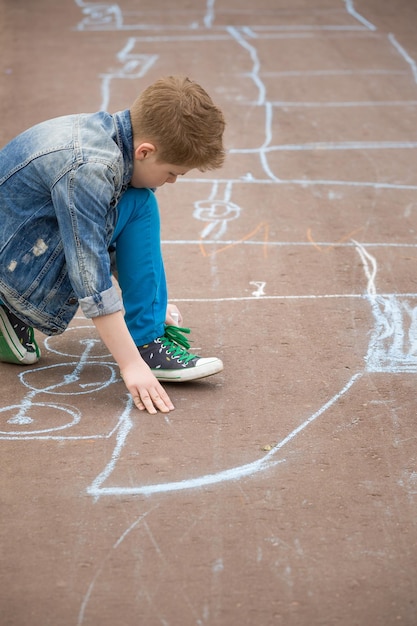 Cute kid boy drawing with chalk on the pavement in the park\
summer activities for children creative child drawing with blue\
chalk on the road