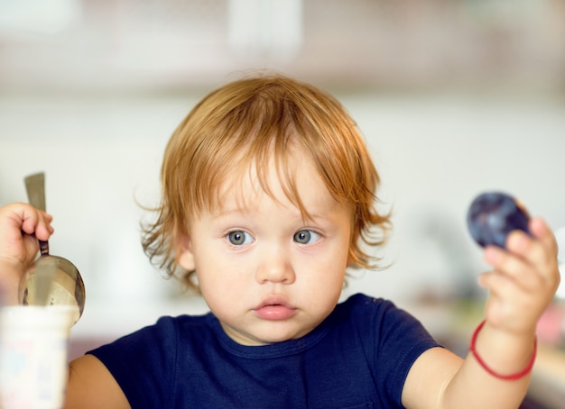 Cute kid boy eating yogurt and plums