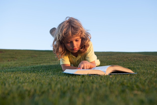 녹색 잔디에 귀여운 꼬마 소년 읽기 책 재미 있는 아이 봄 공원에서 책을 읽고