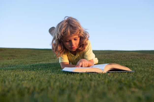 Cute kid boy reading book on green grass funny child reading the book in spring park