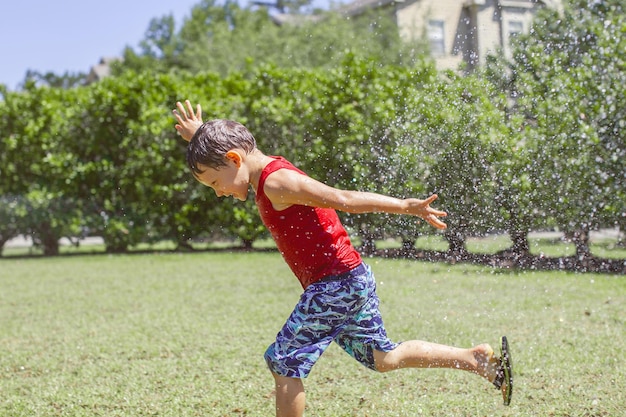 Cute kid boy splashing with gardening hose on backyard on\
summer day