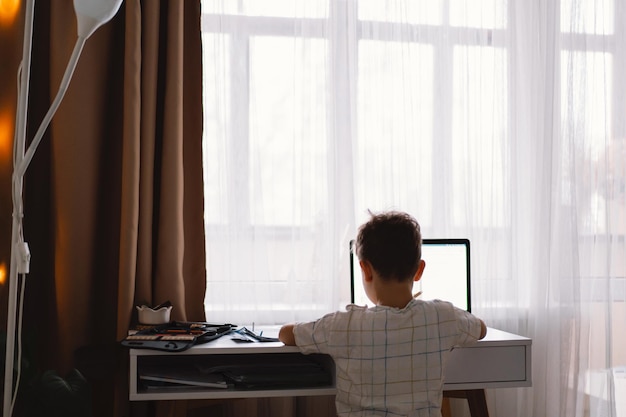 Cute kid boy studying at home with laptop and doing school homework