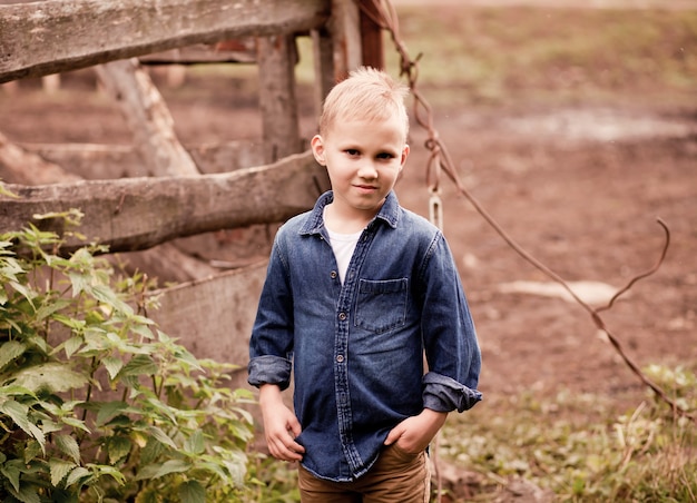 Cute kid cowboy standing near by wooden fence with horses