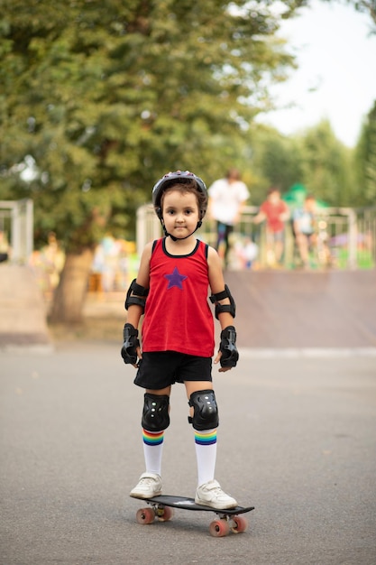 Cute kid girl child with skateboard in a hands standing in a skatepark and smiling Child performs tricks Summer sport activity concept