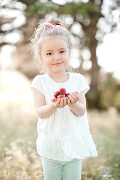 Cute kid girl eating strawberries outdoors