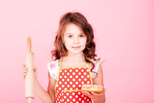 Cute kid girl holding tasty donut over pink background, Unhealthy eating