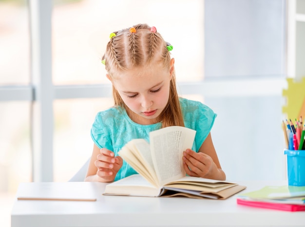 Lettura adorabile della ragazza sveglia del bambino alla tavola