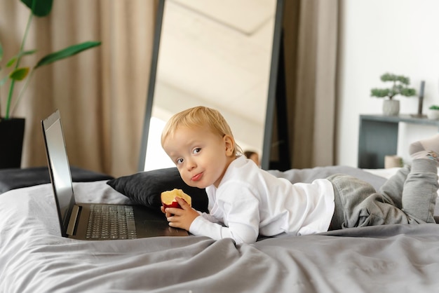 Cute kid is looking at a laptop and holding an apple the rebonk is playing with the laptop a smiling