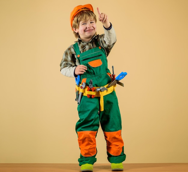 Фото Милый ребенок-ремонтник в защитном шлеме с ремнем инструментов игрушечных инструментов для строительства счастливый ребенок-мальчик в униформе и твердой шляпе с инструментами строителя маленький ребенок-строитель играет с игрушечными инструментами для ремонта
