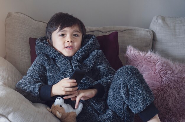 Cute kid sitting on sofa holding remote control