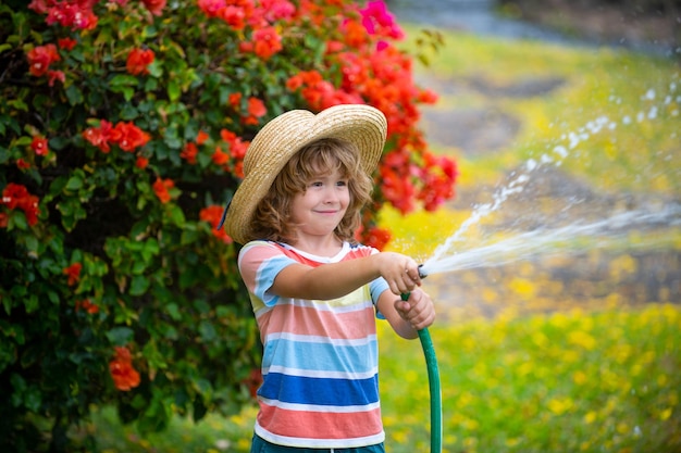 Милый ребенок в соломенной шляпе смеется из шланга для распыления воды