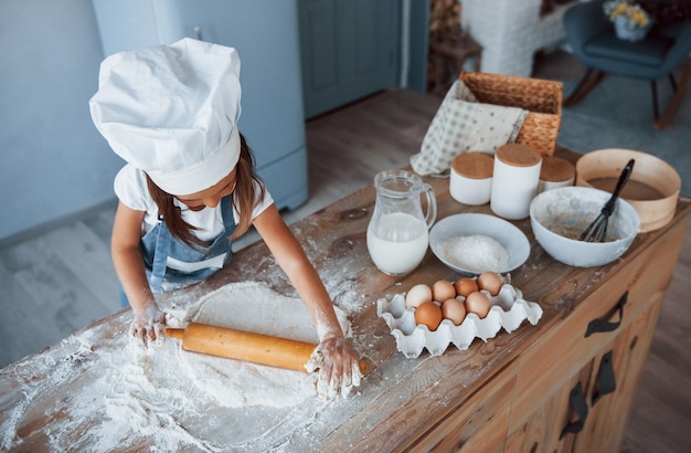 Cute kid in white chef uniform preparing food on the kitchen.