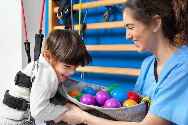 Cute kid with cerebral palsy doing musculoskeletal therapy in the hospital while laughing and having...