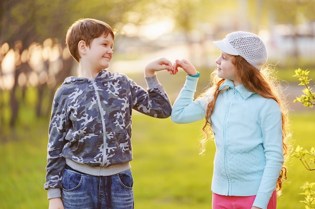 かわいい子供たちは春の屋外でハート形に手を繋いでいます。