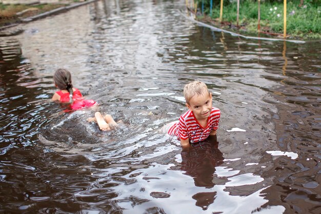 Cute kids jumping and swimming in the puddles after warm summer rain happy childhood