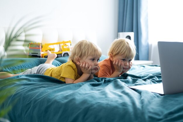 Photo cute kids looking at laptop lying on bed