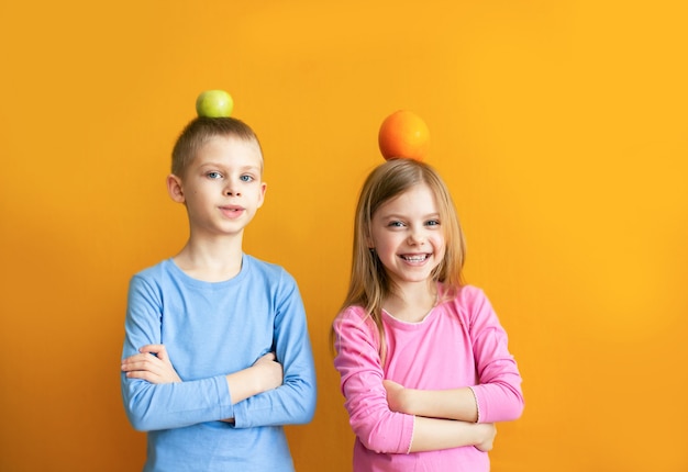 Cute kids on an orange wall with fruit play, put on their heads and laugh