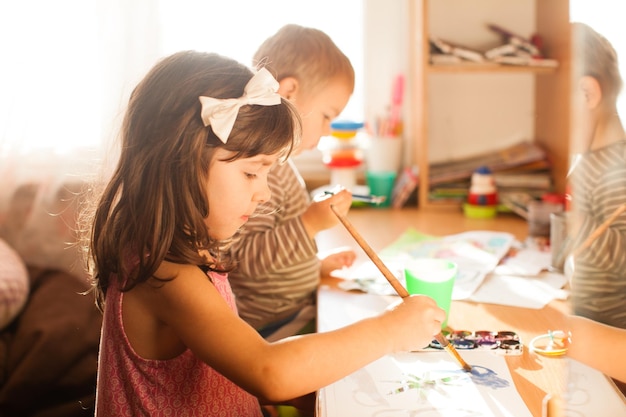 cute kids painting with paintbrush and colorful paints adorable 4 years girl drawing on white paper near window in light room