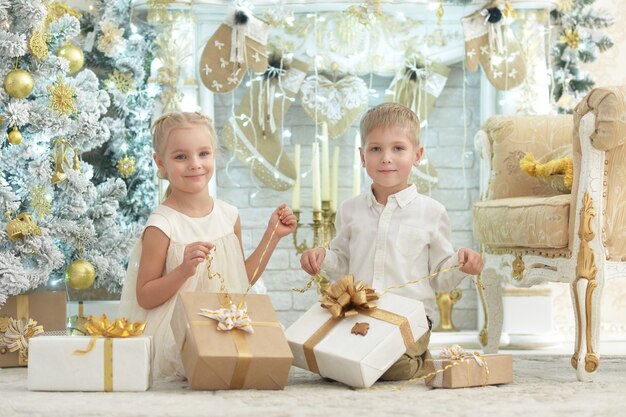 Bambini carini con regali seduti sul pavimento in una stanza decorata per le vacanze di natale