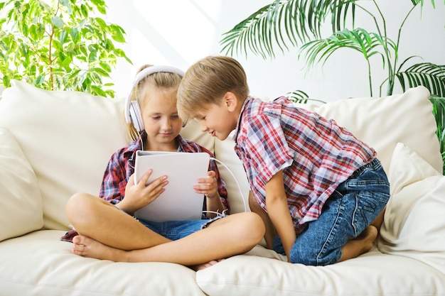 家でタブレットを楽しんでいるヘッドフォンでかわいい子供たち