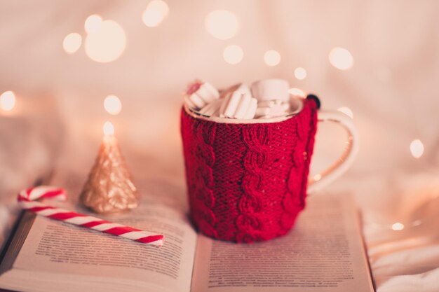 Cute knitted cup of coffee with Christmas candy and tree candle on open book.