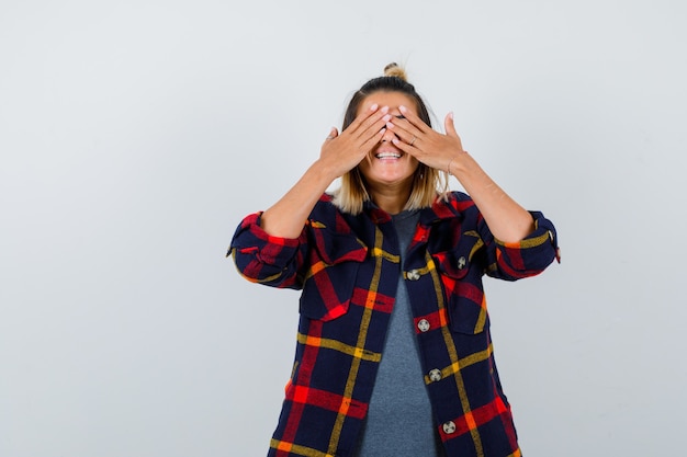 Cute lady covering eyes with hands in checked shirt and looking glad