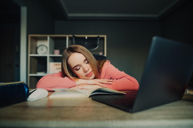 Cute lady sleeps at home at her desk among books while studying online on the Internet