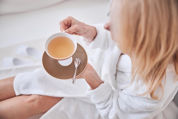 Cute lady with cup of drink in hand spending time in beauty spa salon