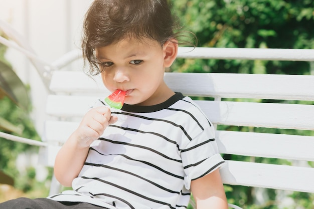 Cute latin indian kid child eating sweet fruit ice cream sitting outdoor colorful lovely