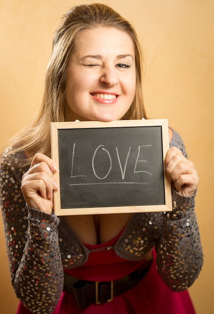 Симпатичная смеющаяся женщина позирует со словом «любовь», написанным на доске