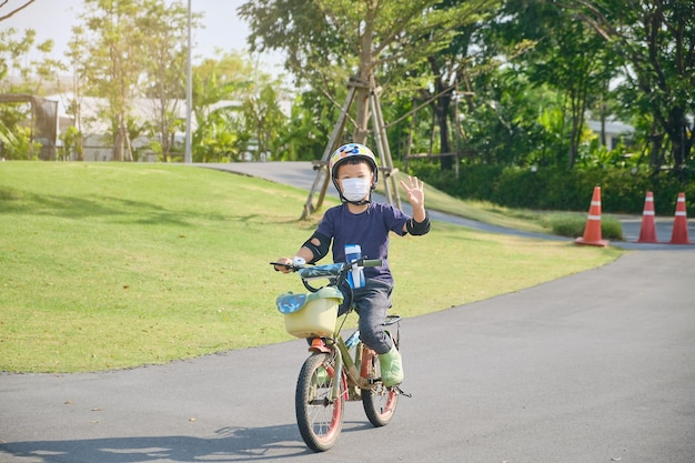 Photo cute little 5 years old toddler boy child in safety helmet wearing medical face mask riding a bike on nature kid cycling playing outside at park fun exercise for kids new normal lifestyle concept