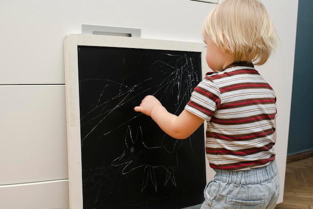 Foto carino piccolo adorabile ragazzo caucasico disegni gesso sulla lavagna a casa babys mani pittura creativa divertente attività al coperto per lo sviluppo dei bambini infanzia asilo nido concetto