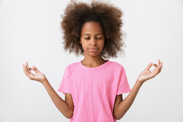 Cute little african girl wearing pink blouse standing isolated over white wall, meditating