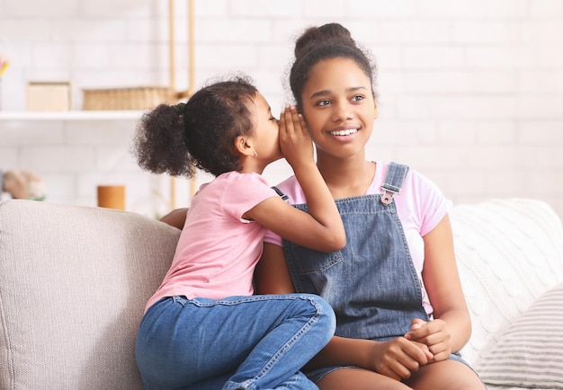 Cute little african girl whispering something to her elder sister ear